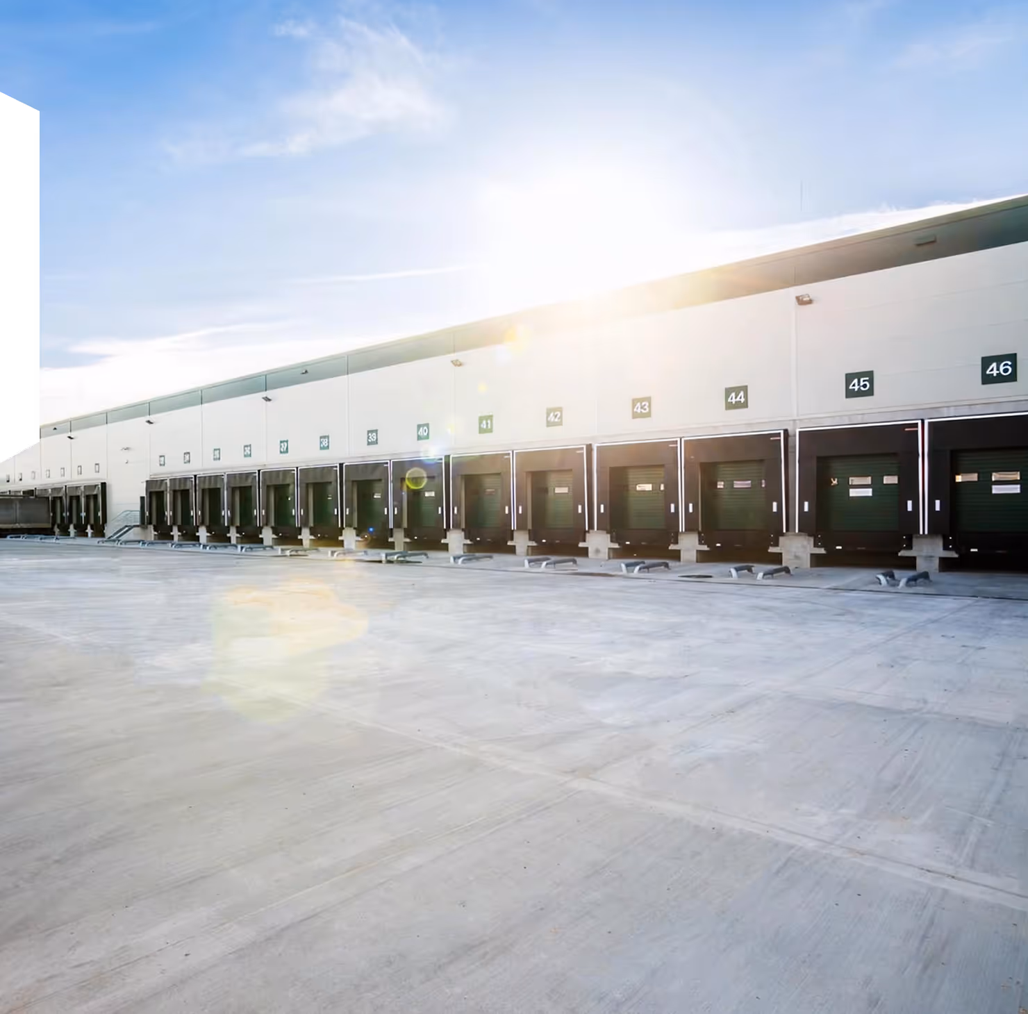 Long row of loading dock doors numbered 27 to 46 on a warehouse building under a bright sun.